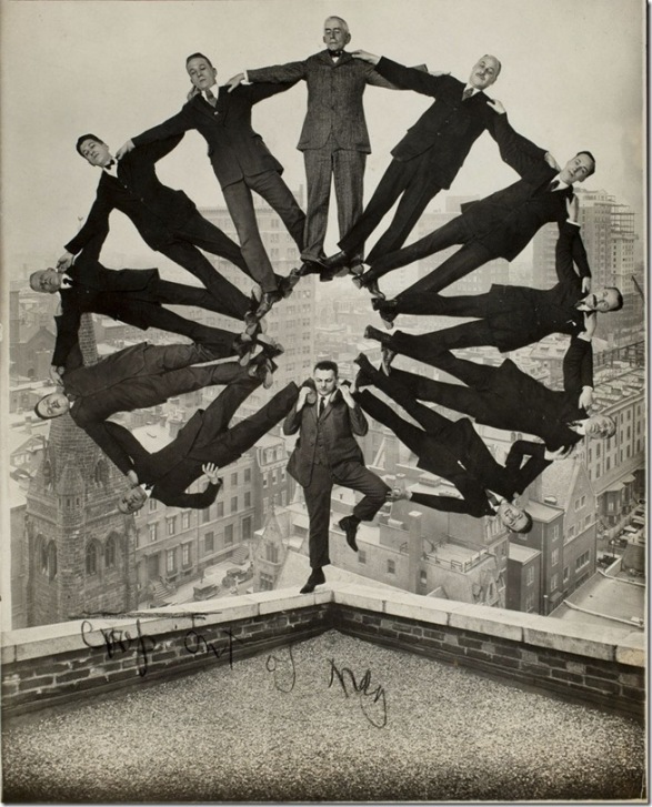 Trick photo of man standing on edge of building with 11 men  in formation on his shoulders